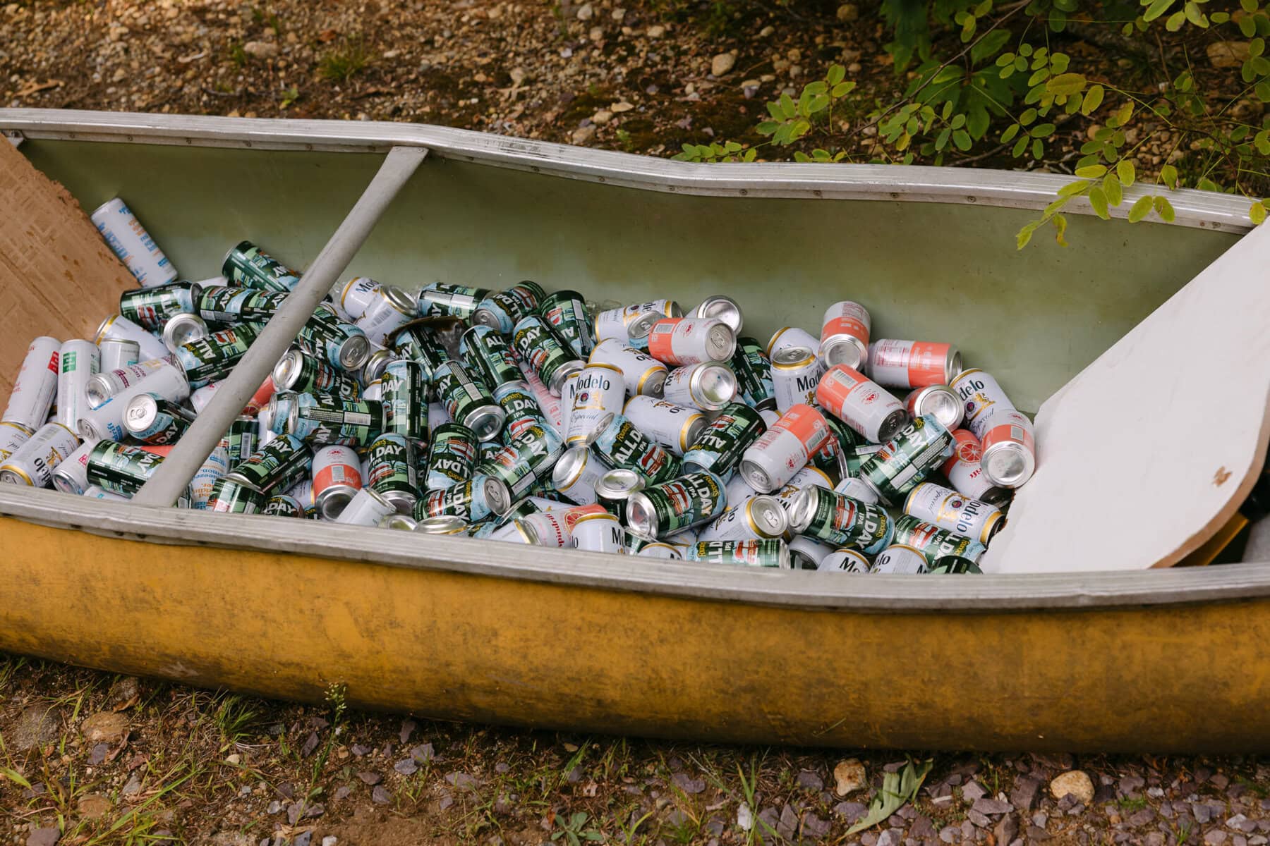 A Worcester Wedding at Cook Pond 57 A yellow canoe on the ground at Cook Pond is filled with empty beer and soda cans.
