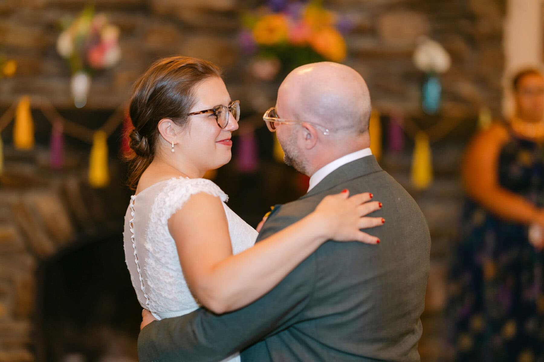 A Worcester Wedding at Cook Pond 86 A couple dressed formally dances together indoors, with a stone wall and colorful decorations at a charming Worcester Wedding.